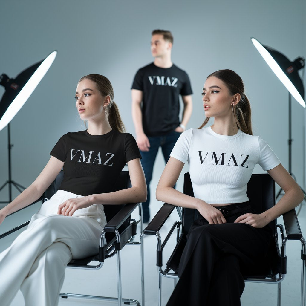 Two models wearing VMAZ branded T-shirts sitting on chairs under studio lights, fashion photoshoot background.